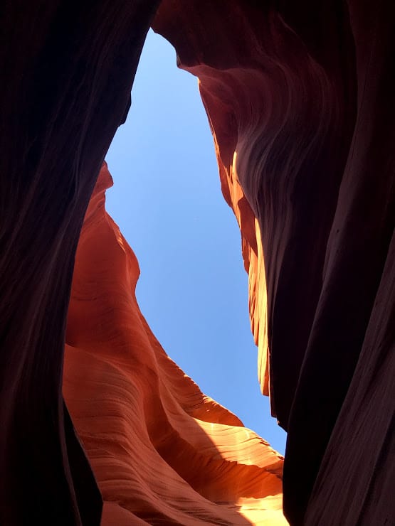 a slash of blue sky view from the bottom of Antelope Canyon with warm red walls glowing in the light 