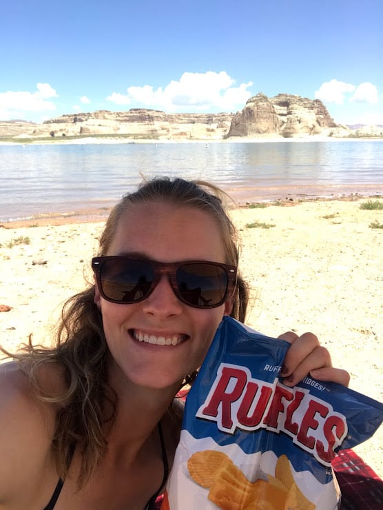 A blonde woman (me) smiling and holding a Ruffles Chip bag with Lake Powell in the background 