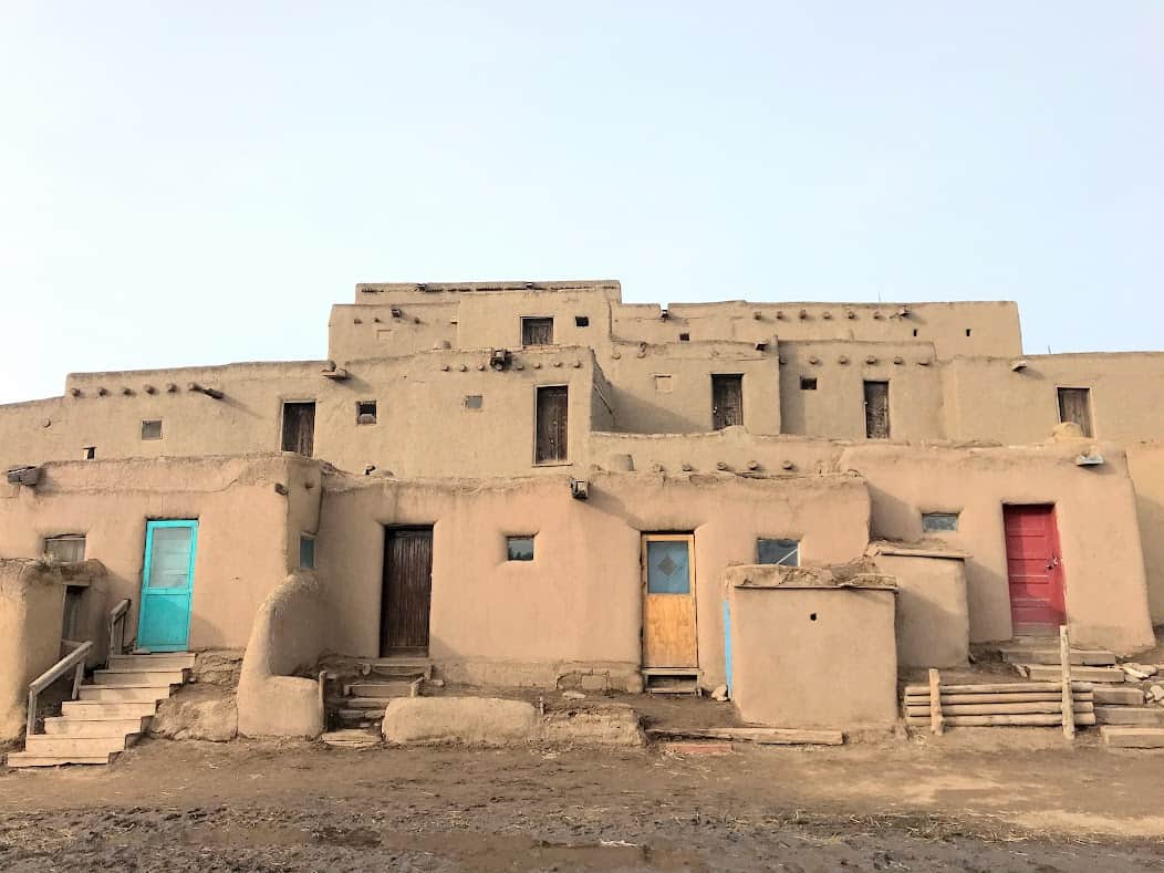 A group of multistoried pueblo style brown buildings with brightly colored doors against a blue sky