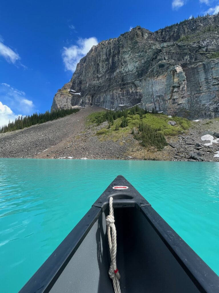 the bow of a canoe on the waters of Lake Louise with a mountain and talus field in the background