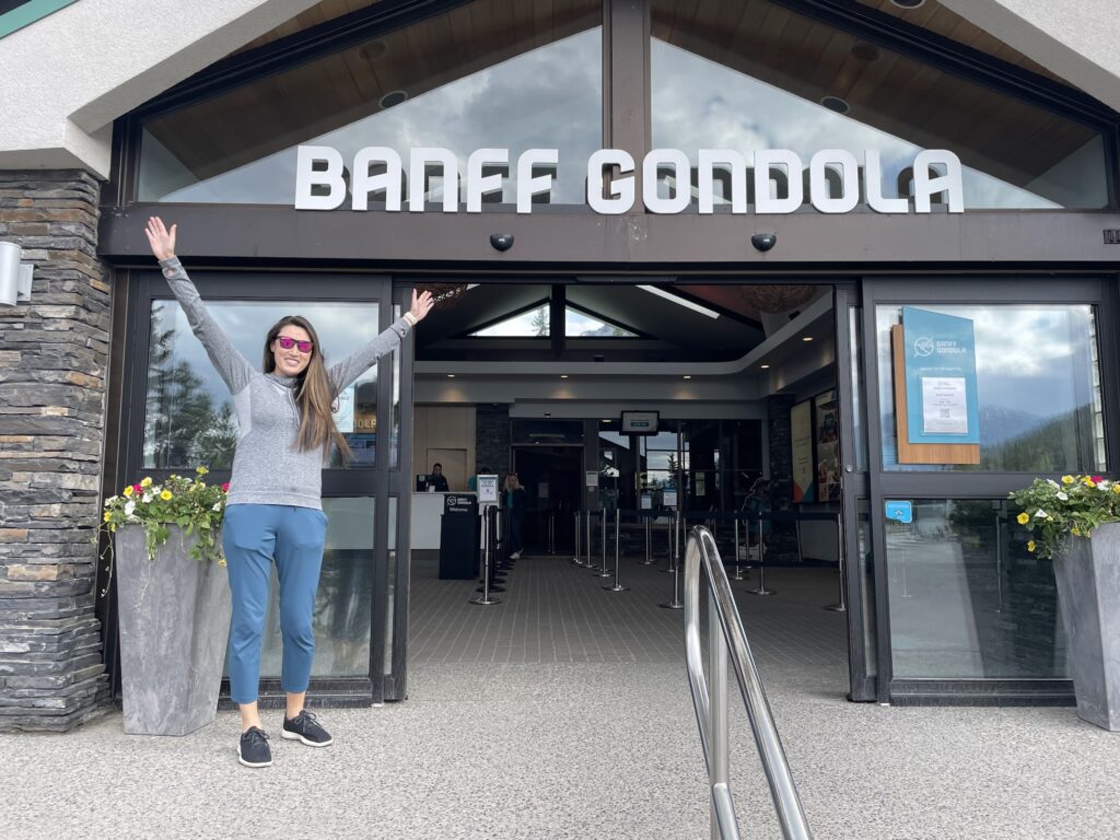 a girl stands in front of the Banff gondola ticket office 
