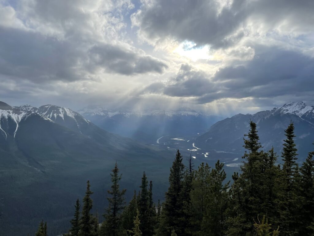 sun streams through the clouds illuminating the Bow River and mountains from the Banff Gondola viewpoint