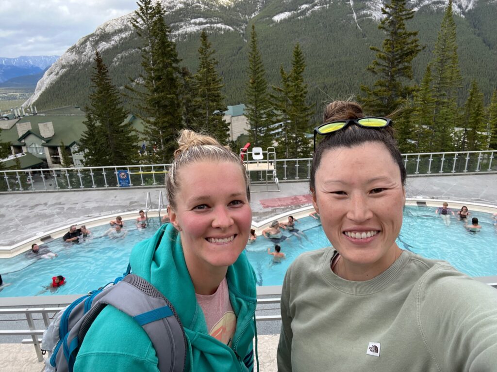 The author and friend take a selfie in front of a busy Banff Upper Hot Springs 
