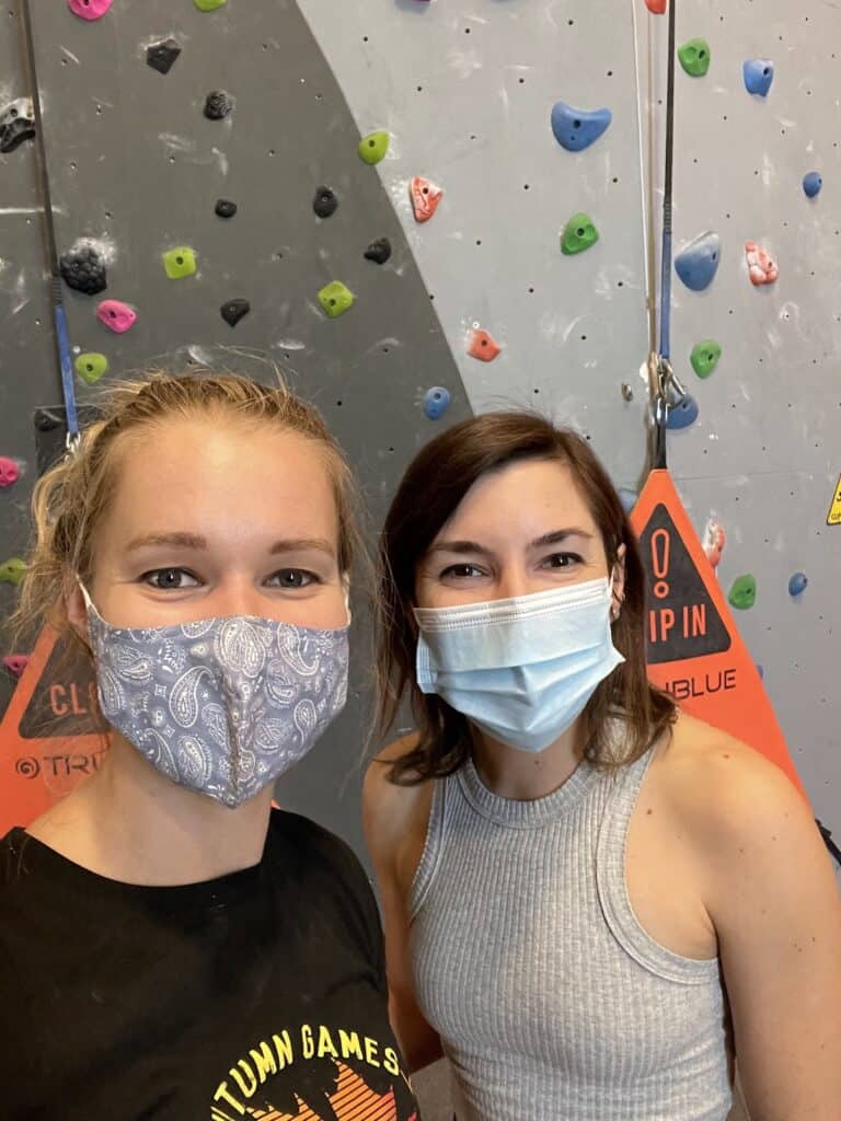 two women wearing masks smile? for the camera after a fun day of indoor rock climbing