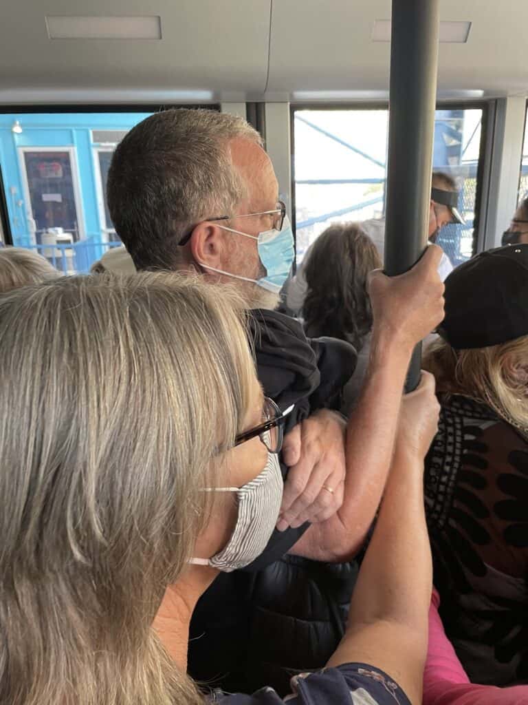 a close-up view of the inside of the tram as riders hold onto the poles and are packed shoulder to shoulder inside the tram