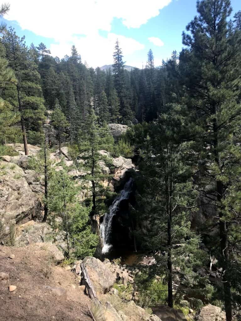 A small waterfall flows down the rocks, surrounded by green pine trees. Jemez Falls is one of the perfect day trips from Albuquerque
