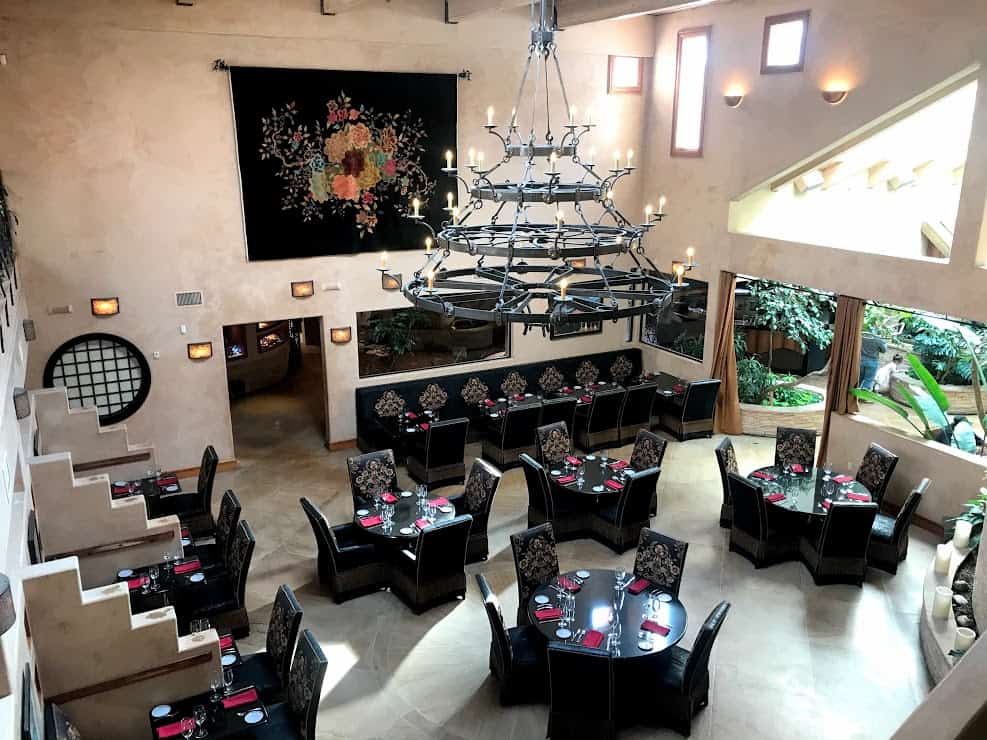 A pueblo style dining room with a wrought iron chandelier and ornate black tables set underneath it