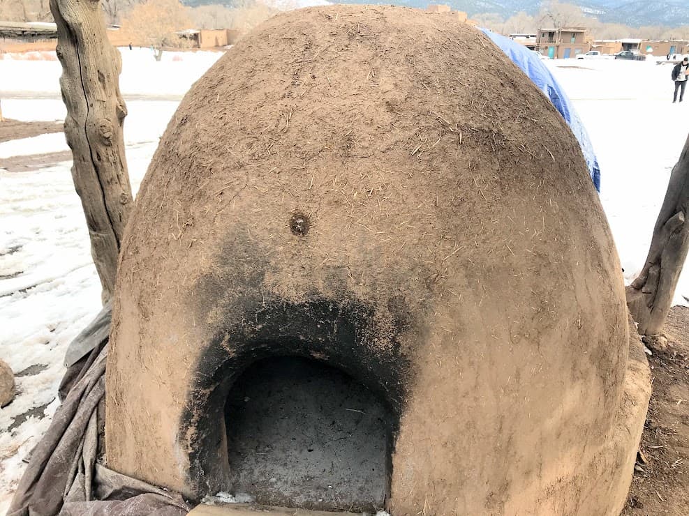 An adobe dome with an opening cut in it, blackened from use as an oven 