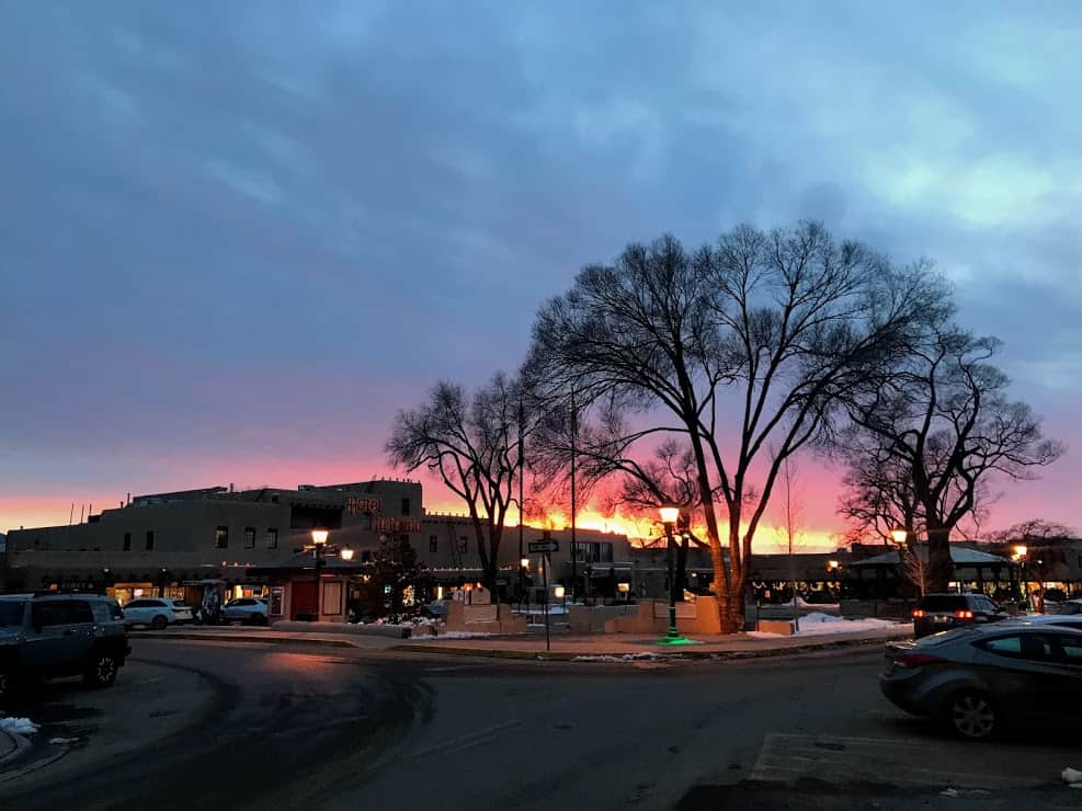 a pink and purple sunset behind the silhouette of a tree in the dimly lit plaza of Taos