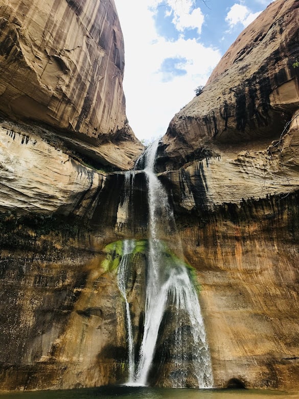 a waterfall pours down a tan rockface, splitting into a separate stream of water at Lower Calf Creek Falls in Utah