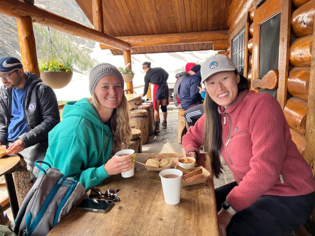 the author and friend sitting at a wooden table at the Lake Agnes Tea House enjoying tea and biscuits