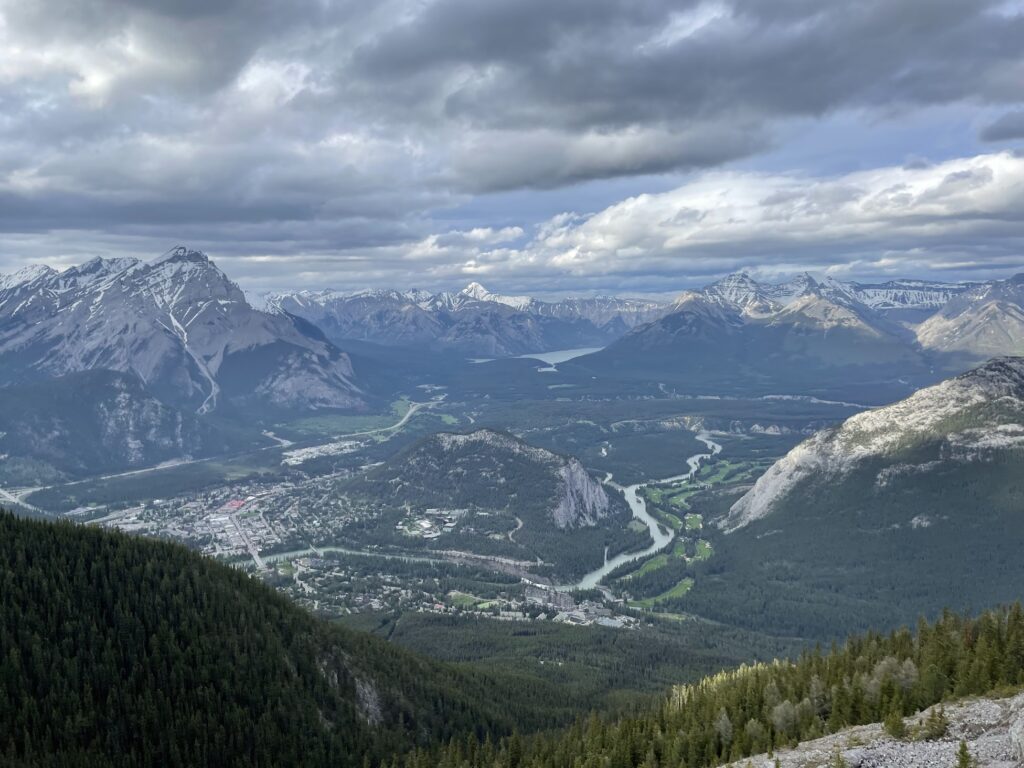 view from the top of Sulphur Mountain in Banff, Canada. the Bow River flows through the valley and a golf course is visible near the town.