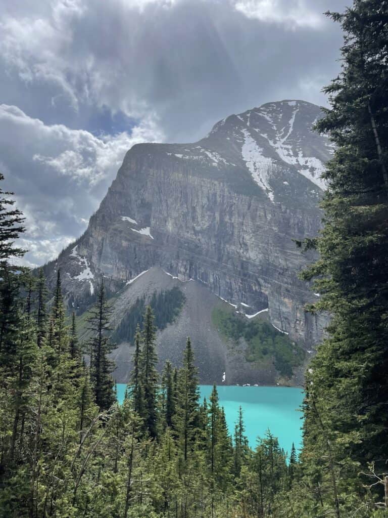 Lake Louise glowing turquoise with a huge mountain towering above it on a cloudy day