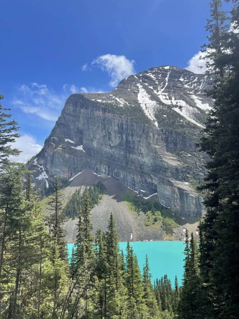Lake Louise glowing turquoise with a huge mountain towering above it on blue sky day