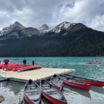 four red canoes float in the water of Lake Louise next to the dock