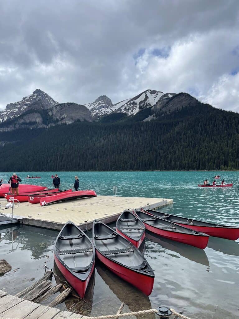 four red canoes float in the waters of Lake Louise next to a floating dock. 