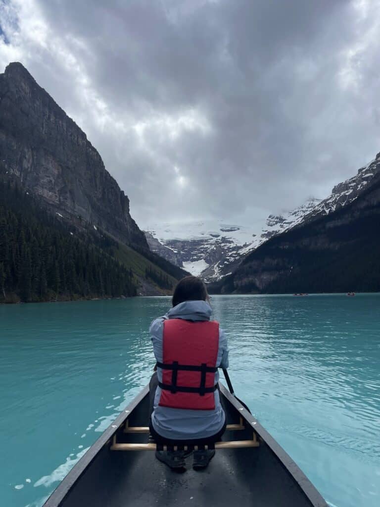 a woman in a canoe on Lake Louise. Her back is to the camera and she is looking off at a snow-covered mountain