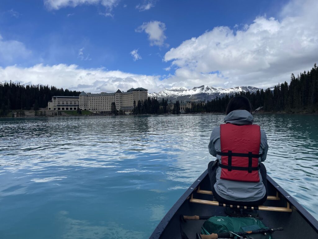 a woman sits in a canoe on Lake Louise with her back to the camera. Her head blends into the trees so she almost looks headless.