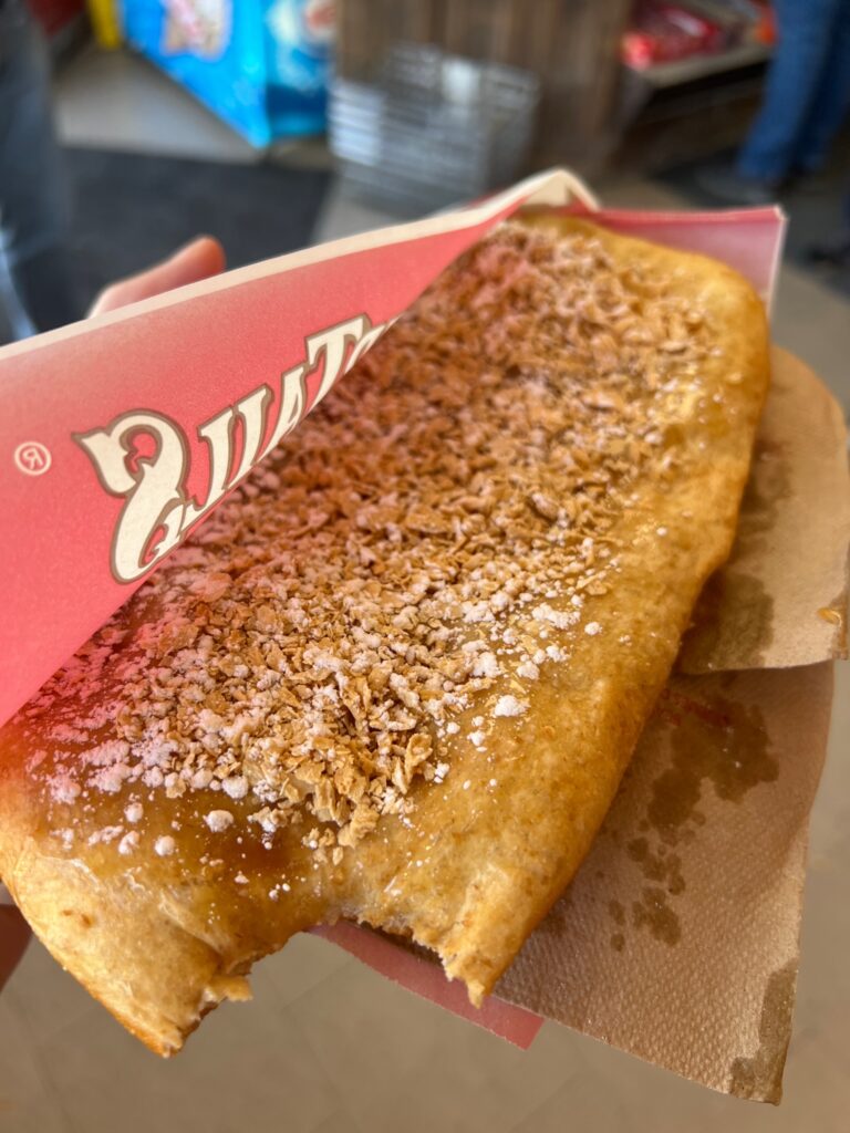 a close up of a large fried pastry called a beaver tail, with powdered sugar, syrup and maple crumbs