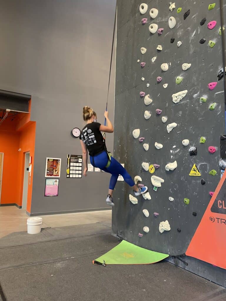 a blond woman rappelling down a wall in an indoor rock climbing gym 