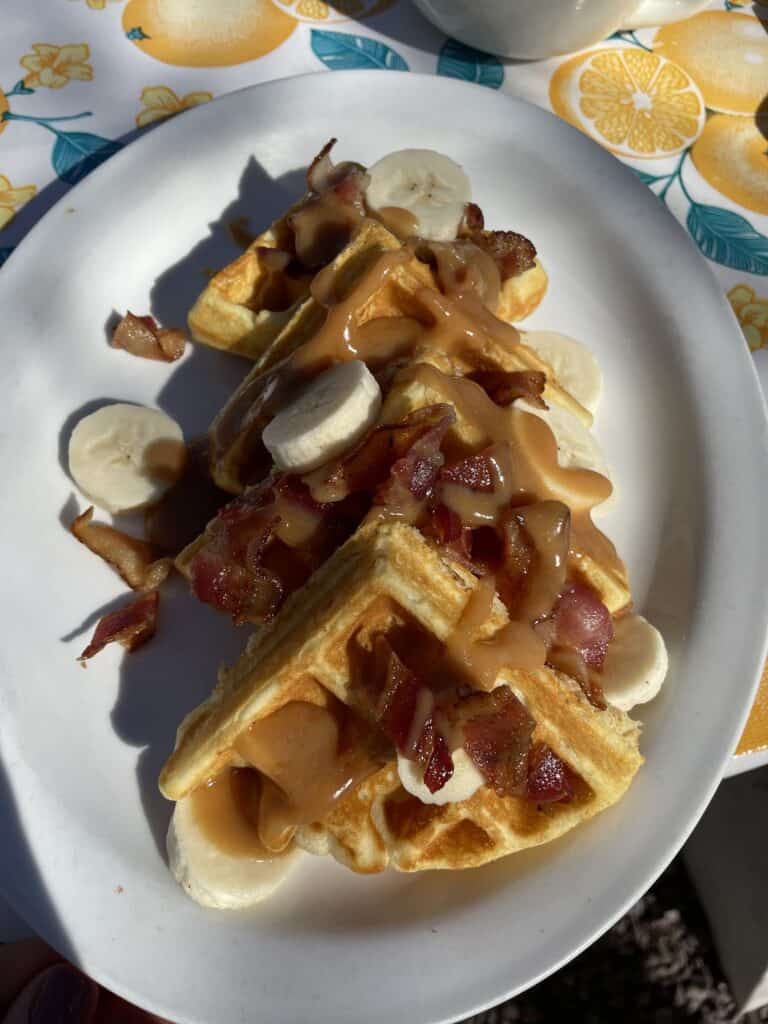 a plate of waffles drizzled in peanut butter, covered in bacon and bananas from one of the best breakfast spots in Albuquerque: Tia B's waffleria