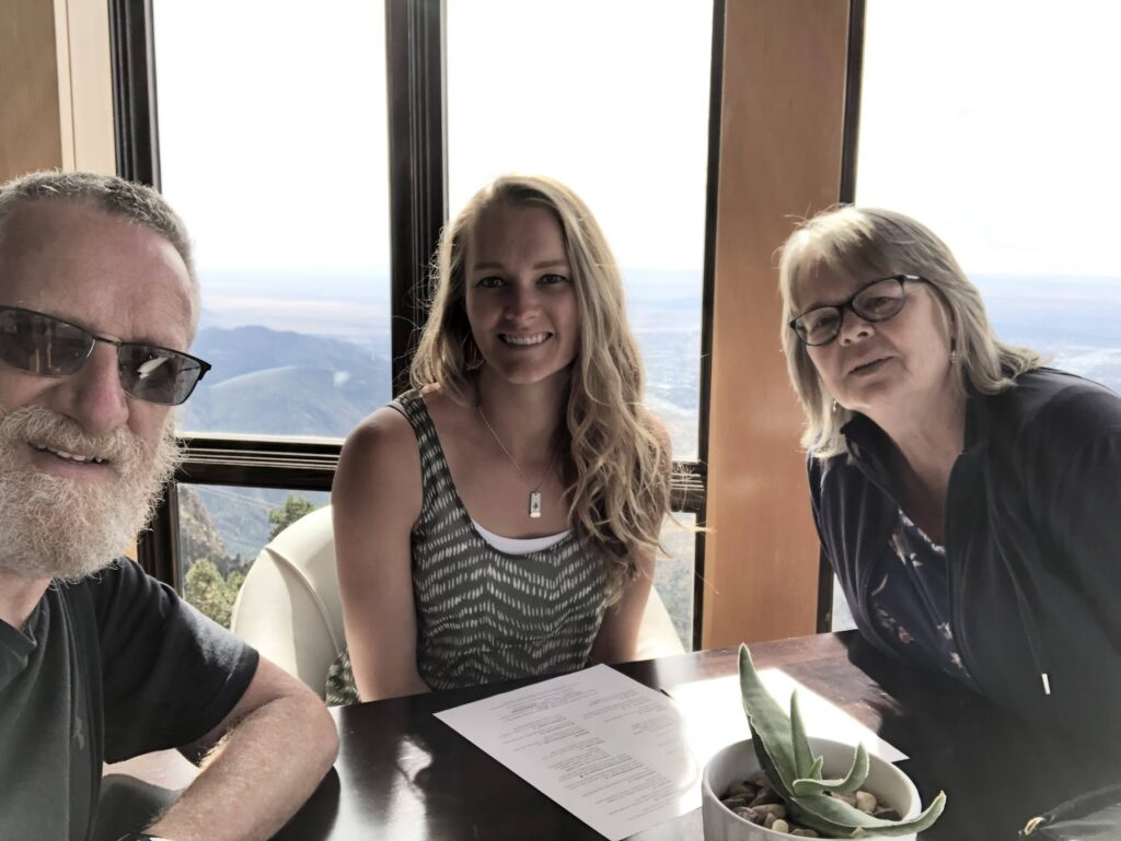 the author and her parents sit at a table at Ten3 restaurant, with the view from the mountaintop behind them