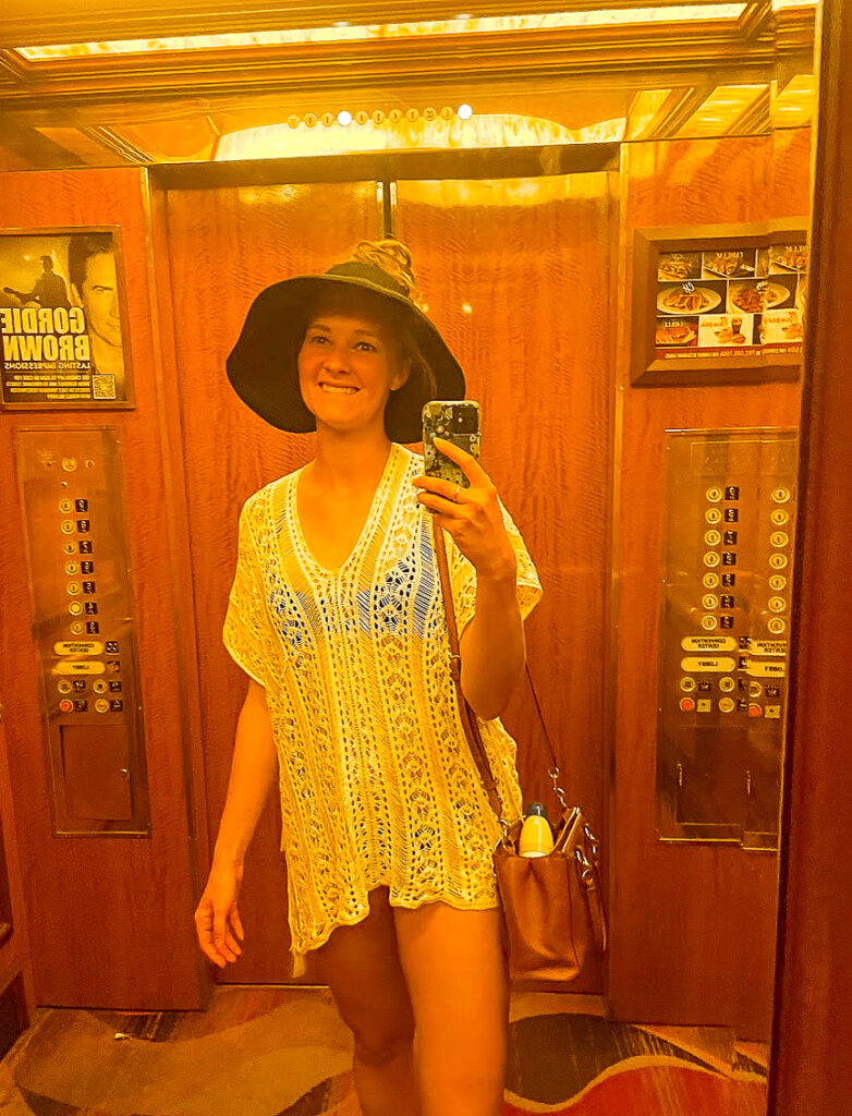 a woman smiles in a swimsuit cover-u and black sun hat inside of an elevator