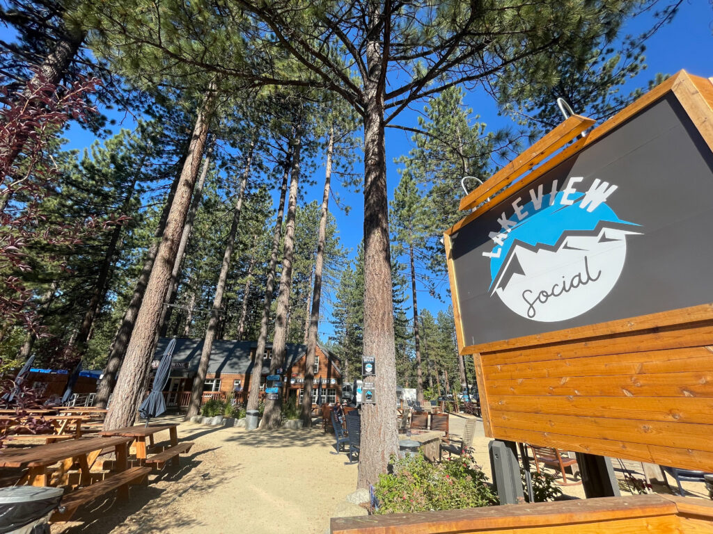 picnic tables under towering trees next to the Lakeview Social sign 